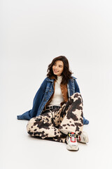 Stylish young woman showcases trendy cow print pants with denim jacket in studio setting