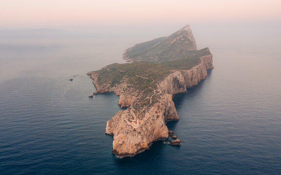 Aerial view of Dragonera Island's rugged cliffs meet the tranquil, deep blue sea under a soft, hazy sky, Parc Natural de Sa Dragonera, Balearic Islands, Spain.