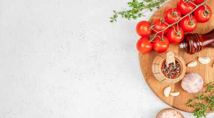 Fresh cherry tomatoes on the vine with garlic, peppercorns, herbs, and pink salt on a wooden board. copy space, top view