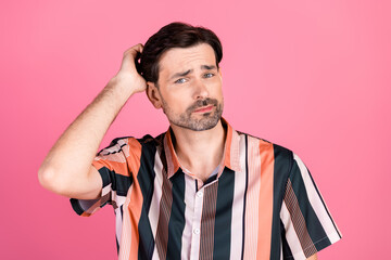 Stylish young man in a striped shirt posing against a pink background, showcasing a thoughtful hand...