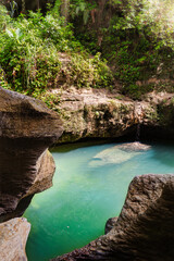 Naklejka premium A serene natural pool surrounded by rocky cliffs and lush greenery, with sunlight illuminating the turquoise water at Charco Azul, Puerto Rico.