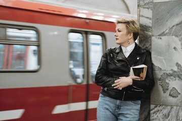 short haired caucasian woman wearing leather jacket looking at coming train at metro station.Image with selective focus, motion effect