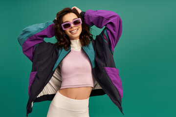 Trendy young woman in sporty outfit poses with confidence against a turquoise backdrop