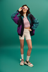 Stylish young woman in trendy sportswear poses against turquoise backdrop