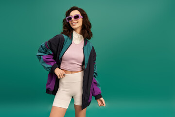 Stylish young woman showcasing trendy sporty outfit against vibrant turquoise backdrop