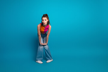 Young stylish woman in colorful outfit posing playfully against vibrant blue background, showcasing...