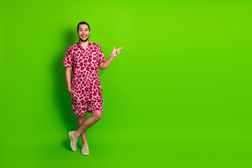 Cheerful trendy man in pink leopard print outfit gesturing against bright green background...