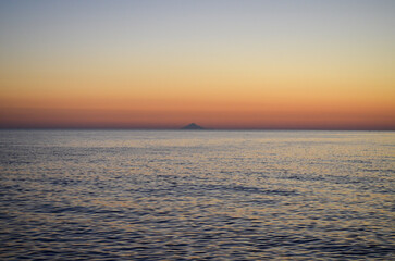 The ocean is calm and the sky is a beautiful orange color. The sun is setting, creating a warm and peaceful atmosphere