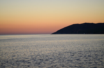 The ocean is calm and the sky is a beautiful orange color. The sun is setting, creating a warm and peaceful atmosphere