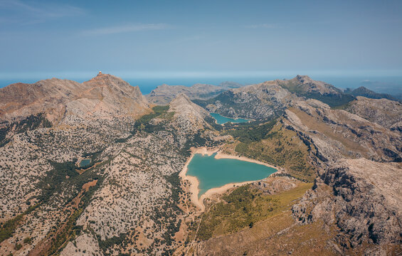 Aerial view of a turquoise reservoir nestled amid rugged mountain peaks under a clear sky at Mirador Embassament de C&Atilde;&ordm;ber, Escorca, Balearic Islands, Spain.