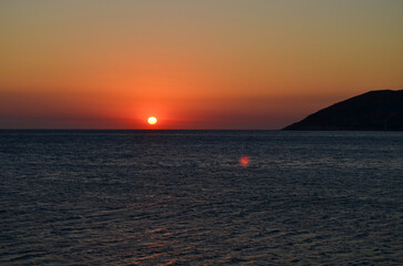 The ocean is calm and the sky is a beautiful orange color. The sun is setting, creating a warm and peaceful atmosphere