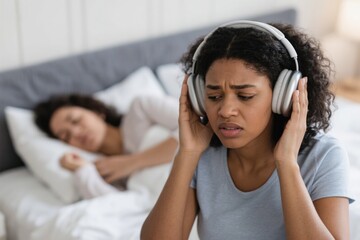 Frustrated Black woman using noise-cancelling headphones while her wif…