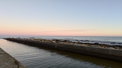 Montevideo. Peaceful coastal landscape with a concrete pier and calm ocean water at dusk. The serene sky shows a beautiful gradient of pink and blue, creating a tranquil and relaxing atmosphere.