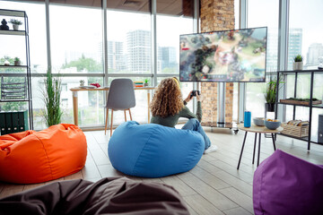 Young woman playing video games in a cozy coworking space with bean bag chairs and modern decor