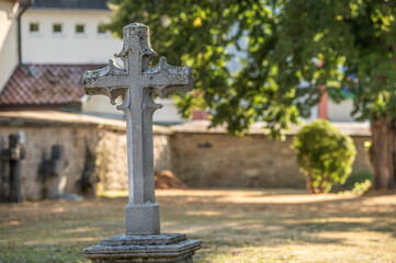 Steinernes  Kreuz in sonnenbeschienenem Kirchhof mit Laubbaum an der Martinskirche in Neckartenzlingen