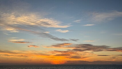 Fototapeta premium Vibrant sunset paints the sky with fiery orange and soft blue hues over a calm ocean horizon