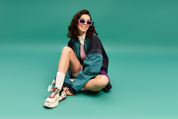 Young stylish woman showcases sporty fashion in vibrant turquoise studio backdrop