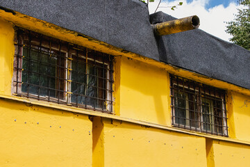Exposed yellow wall with barred windows and rustic charm in a tranquil outdoor setting
