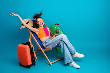 Happy young woman relaxing on a deck chair with sunglass, colorful outfit, and preparing for a tropical summer holiday