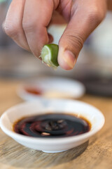 Hands are squeezing green lemon in to a black dip. Close up