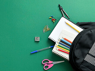 A textured green background with school supplies. Includes a black backpack, colored pencils, scissors, a notebook,