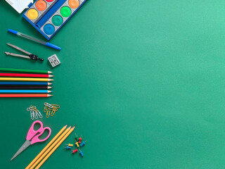 A textured green background with a black backpack and various school supplies including colored pencils, 