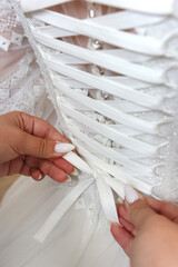 The girls help the bride lace up the corset of her wedding dress.