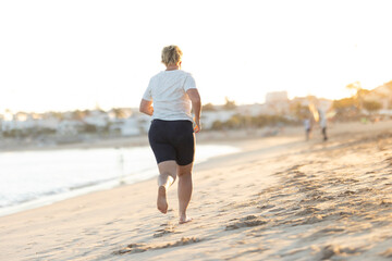Woman running barefoot on the beach at sunset