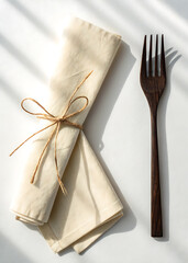 Rustic linen napkin tied with twine next to a dark wooden fork on a white surface