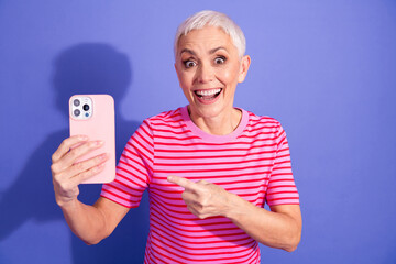 Happy elderly woman with short grey hair wearing a striped t-shirt and holding a smartphone in...