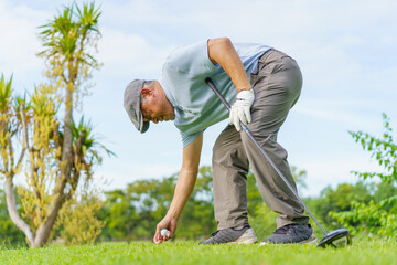 Elderly Asian man enjoying the morning round of golf in soft and warm sunlight.