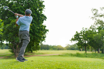 Elderly Asian man enjoying the morning round of golf in soft and warm sunlight.