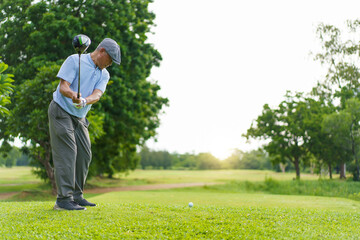 Elderly Asian man enjoying the morning round of golf in soft and warm sunlight.