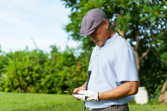 Elderly Asian man enjoying the morning round of golf in soft and warm sunlight. - Powered by Adobe