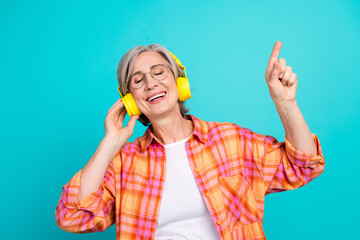 Happy mature woman listening to music with headphones, enjoying and dancing against a cheerful turquoise background