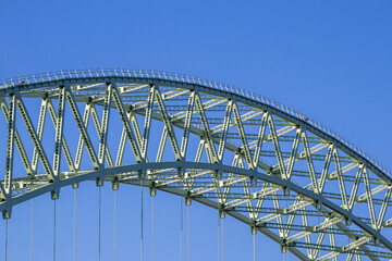 Close-up of green steel truss arch structure of a suspension bridge under blue sky