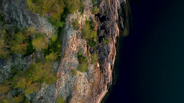 Aerial view of a rugged, rocky shoreline where the land meets the dark water, a rugged landscape with sparse vegetation, Sortavala, Russia.