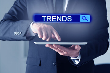 Businessman using tablet computer to find hot tendencies, new ideas, popular directions, closeup. Search bar with word Trends
