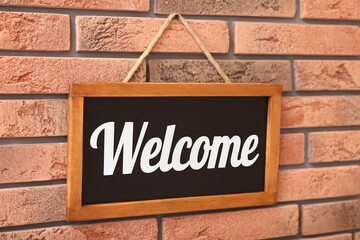 Obraz premium Small chalkboard with word Welcome hanging on brick wall