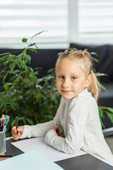 Smiling child girl at desk holding pen and paper. Back to school.