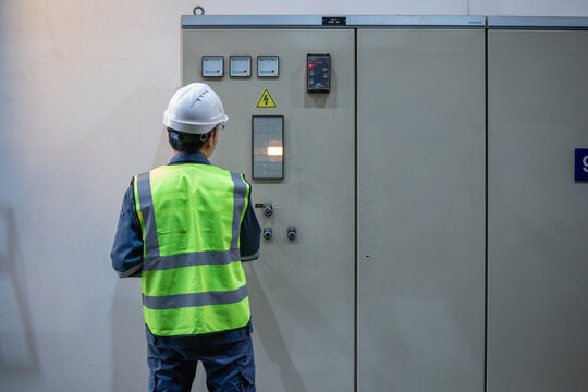 Worker wearing safety helmet and insulated vest operates power switchgear panel inside gas insulated power station, ensuring safe and efficient electrical control