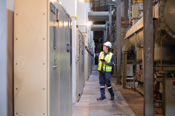 Worker wearing safety gear inspects gas insulated switchgear inside power station with focus and...