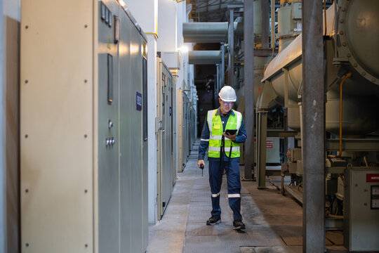 Worker wearing safety gear inspects gas insulated switchgear in power station corridor ensuring operational safety and efficient energy distribution in industrial setting