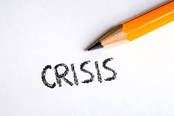 Pencil writing the word "crisis" on a blank white paper. The word is sketched in black, and the pencil rests to the right, symbolizing problems.
