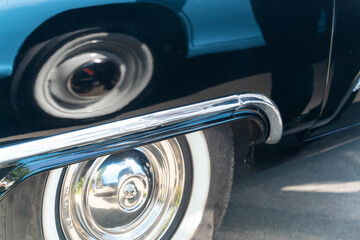 Shiny chrome details and whitewall tire of a classic car reflecting another car's wheel