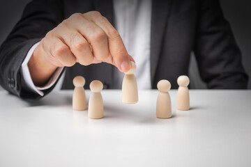 Businessman pick up leads from other wooden dolls on white desk.