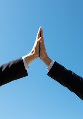 Two business professionals giving a high five, a gesture of celebration for successful teamwork and partnership against a clear blue sky.