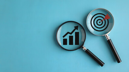 Magnifying glass reveals upward trending growth chart and dart hitting bullseye target, symbolizing business success and strategic planning achievement.