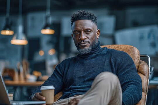 Portrait of a confident African American businessman relaxing in his office, taking a break with coffee and laptop, exuding professionalism and modern style.