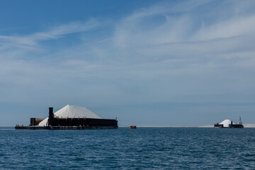 Barges transporting mounds of salt in the sea of cortez, baja california sur, mexico, under a blue sky